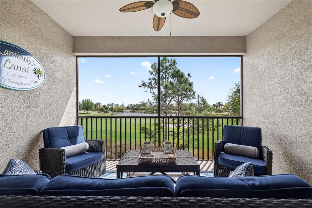 A screened-in lanai with blue patio furniture overlooks a golf course and a lake — 12660 SORRENTO WAY UNIT 204, BRADENTON, FL