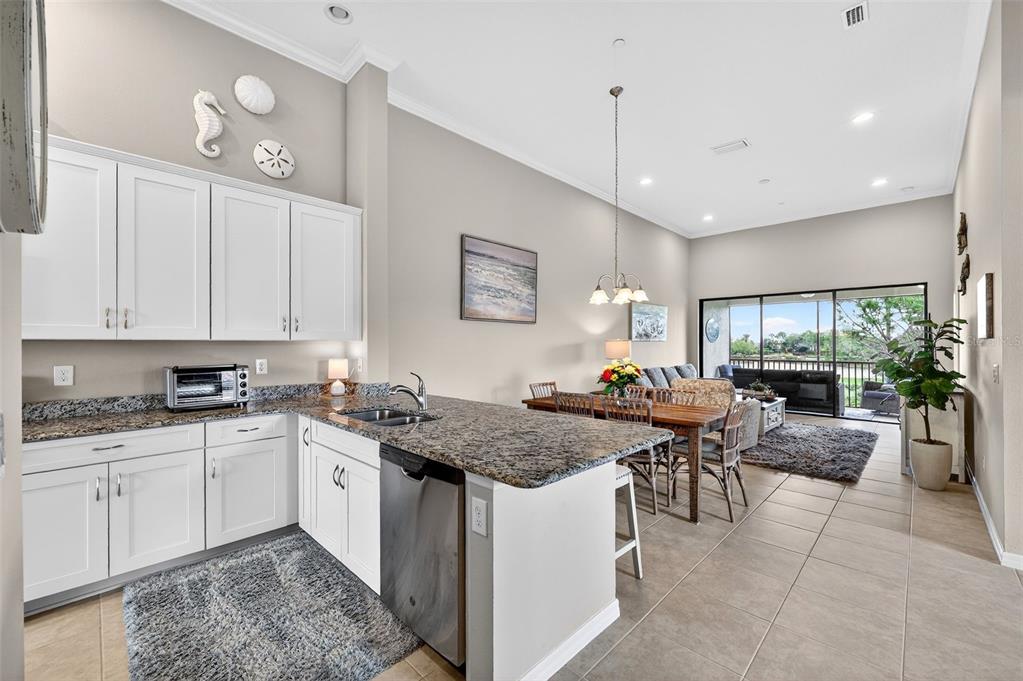 A kitchen with white cabinets and granite countertops opens into a dining and living area — 12660 SORRENTO WAY UNIT 204, BRADENTON, FL