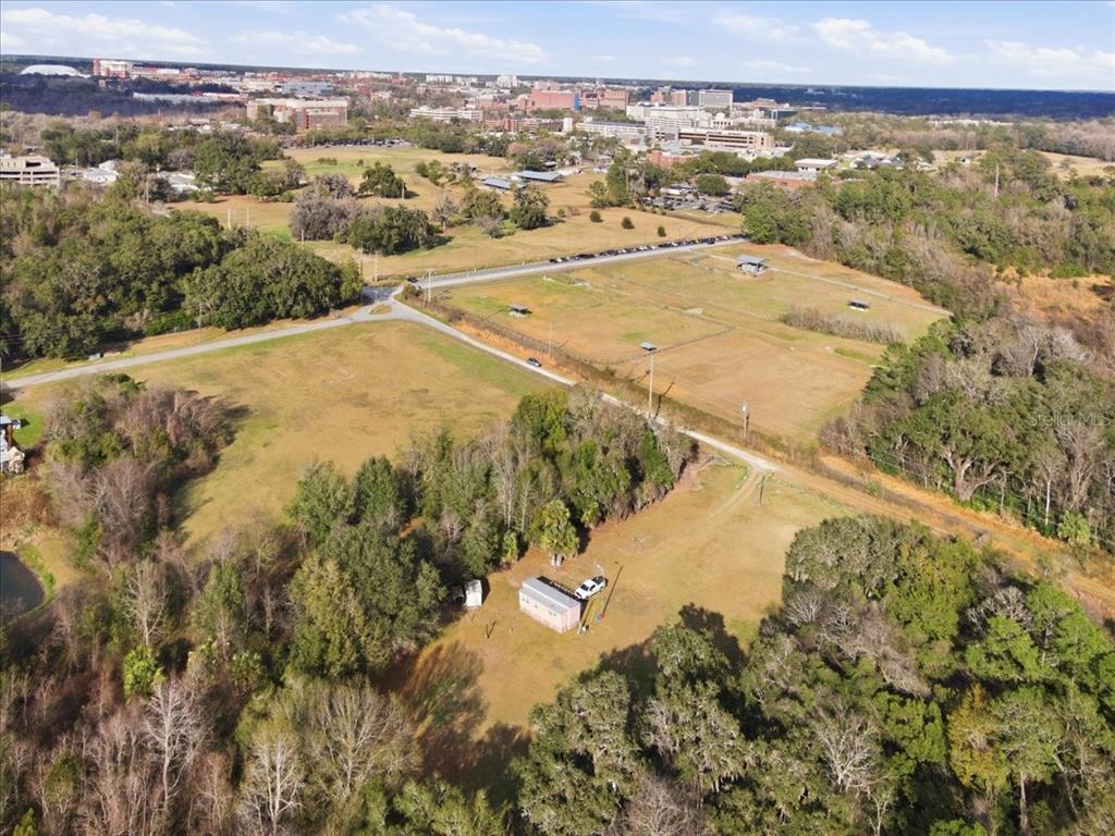 An aerial view shows a small building on a large, grassy lot near a city — 2400 SW 23RD TERRACE, GAINESVILLE, FL