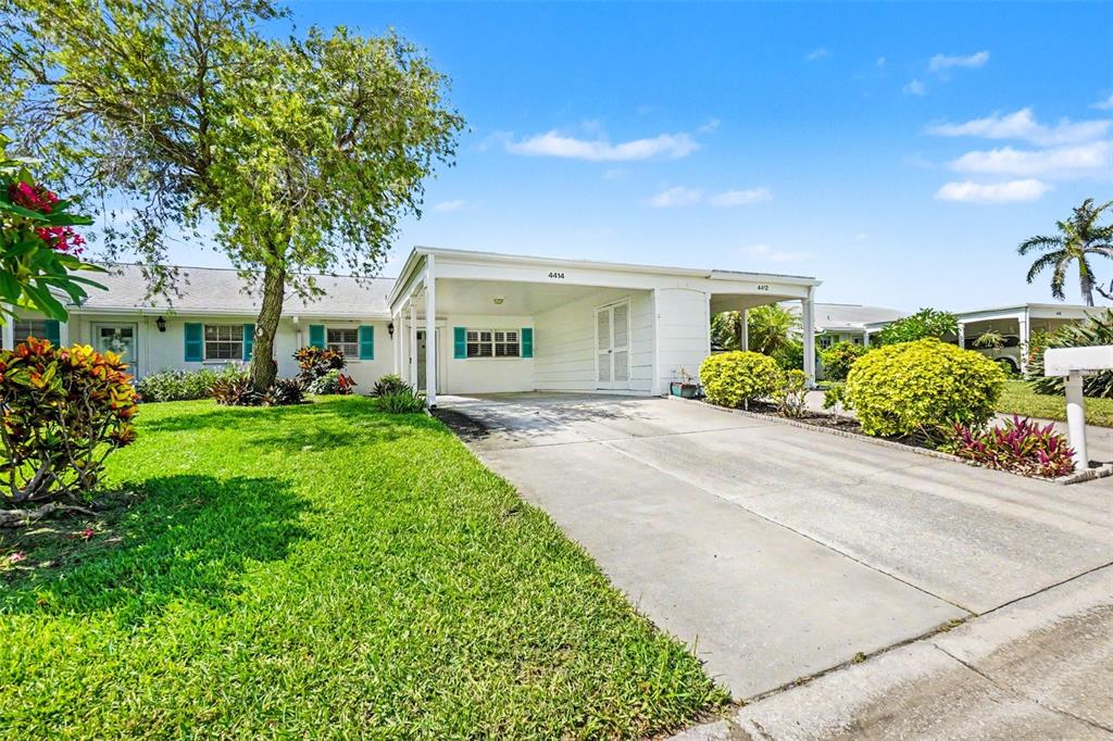 A single-story duplex with white siding, two carports, and a central tree in the yard — 4414 MOUNT VERNON DRIVE UNIT 0, BRADENTON, FL