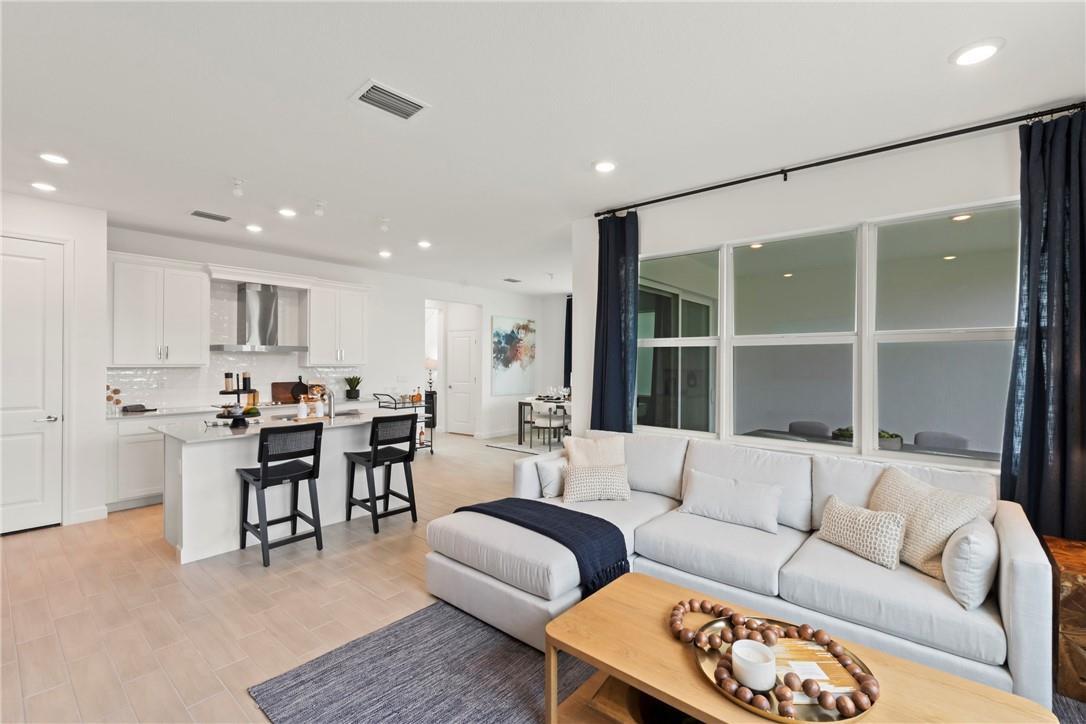 An open-concept living room and kitchen featuring a sectional sofa, island seating, and light flooring — 22812 Caciano Road, Boca Raton FL 33433, BOCA RATON, FL
