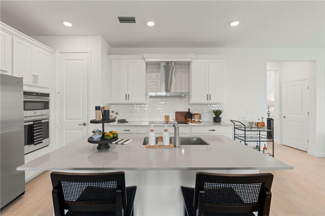 A modern kitchen features white cabinets, a large island with a sink, and stainless appliances — 22812 Caciano Road, Boca Raton FL 33433, BOCA RATON, FL