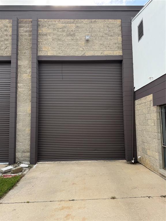 A concrete driveway leads to a large, brown roll-up metal door on a commercial building — 3714 NW 97TH BOULEVARD, GAINESVILLE, FL