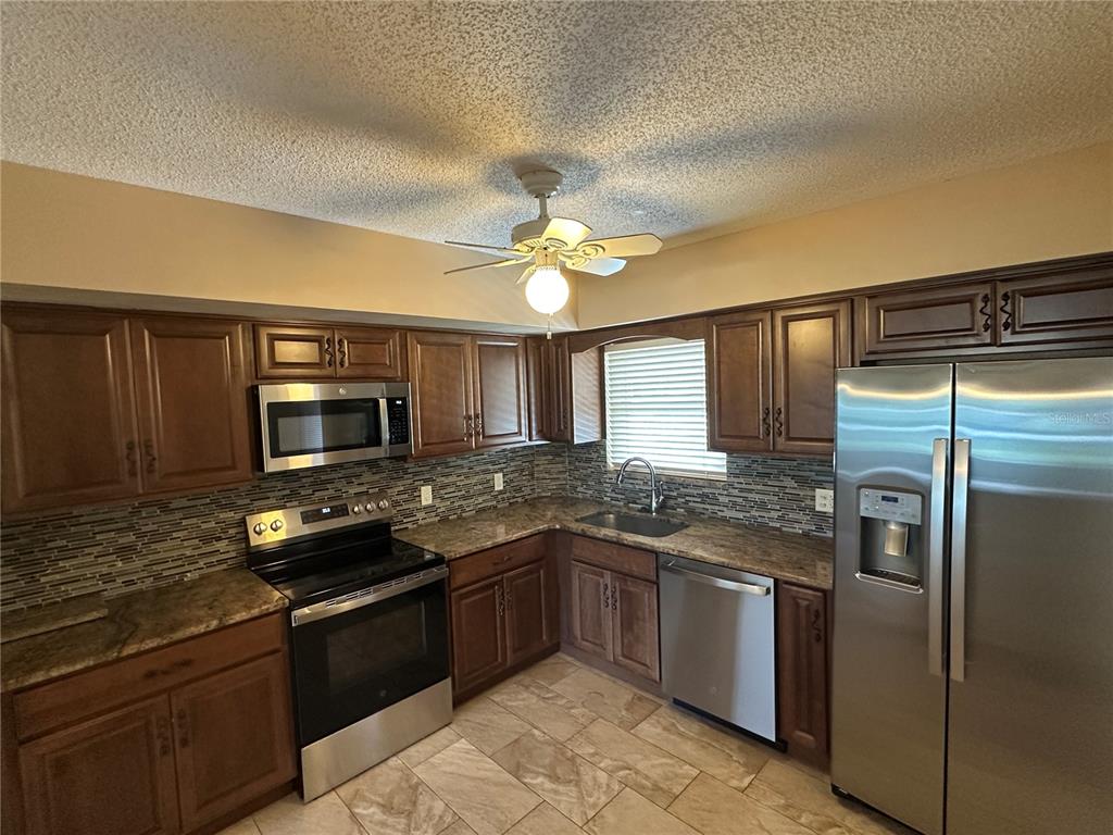 A kitchen features dark wood cabinets, stainless steel appliances, granite countertops, and a tiled backsplash — 2285 ISRAELI DRIVE UNIT 29, CLEARWATER, FL