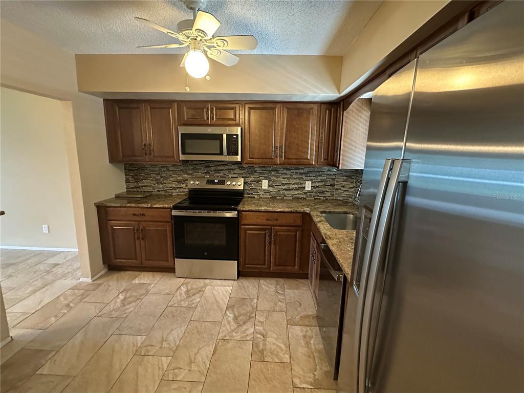 A kitchen features dark wood cabinets, granite countertops, stainless steel appliances, and tiled flooring — 2285 ISRAELI DRIVE UNIT 29, CLEARWATER, FL