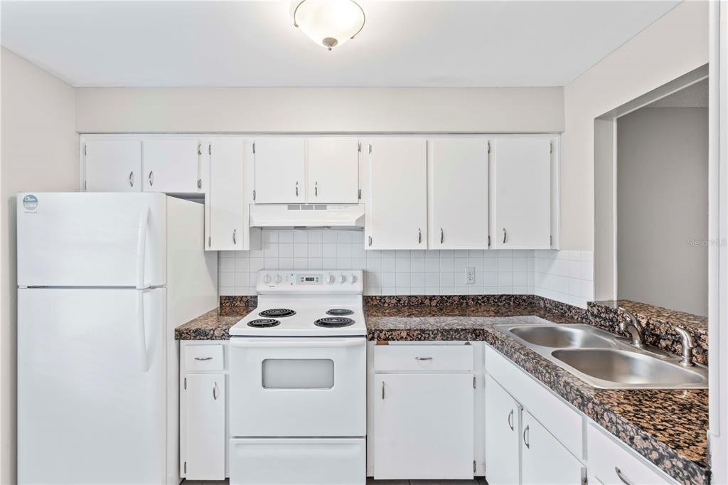 A kitchen features white cabinets, a white stove, a white refrigerator, and dark granite countertops — 11511 113TH STREET UNIT 4F, LARGO, FL
