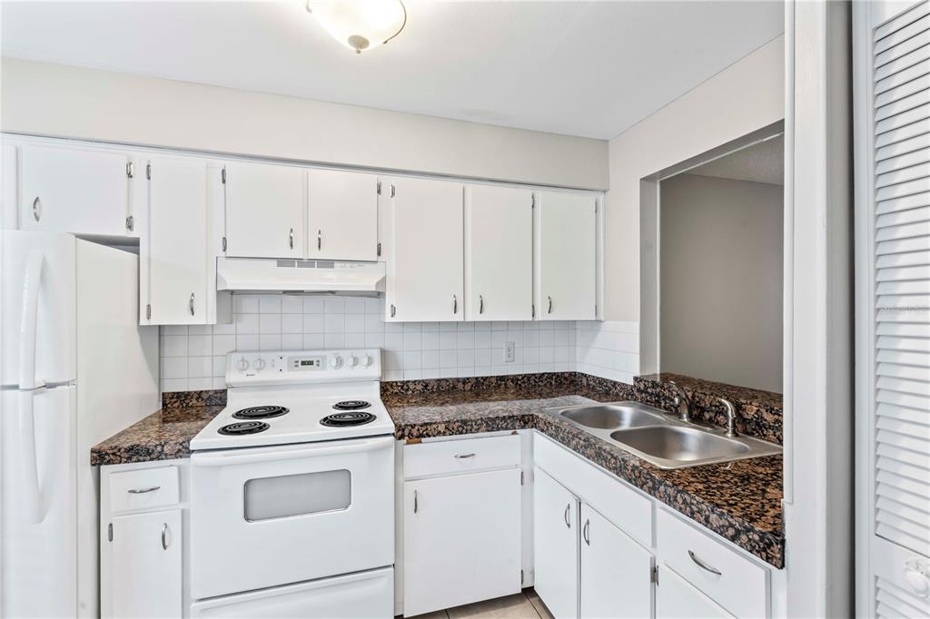 A kitchen features white cabinets, dark granite countertops, a white stove, and a double sink — 11511 113TH STREET UNIT 4F, LARGO, FL