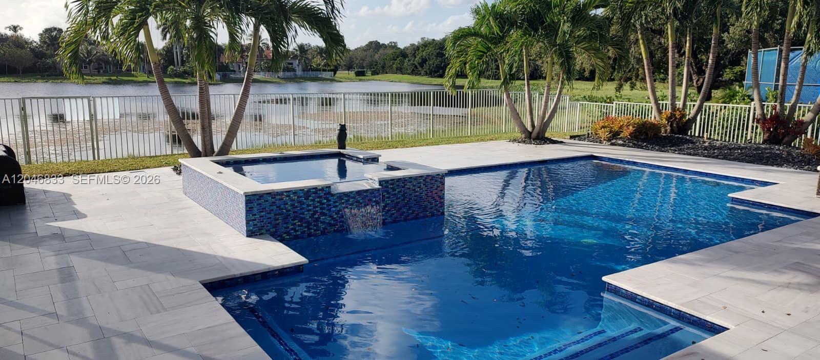 A swimming pool with an attached spa and waterfall feature overlooks a lake and yard — 3683 W Lakes Estates Dr, Davie FL 33328, DAVIE, FL