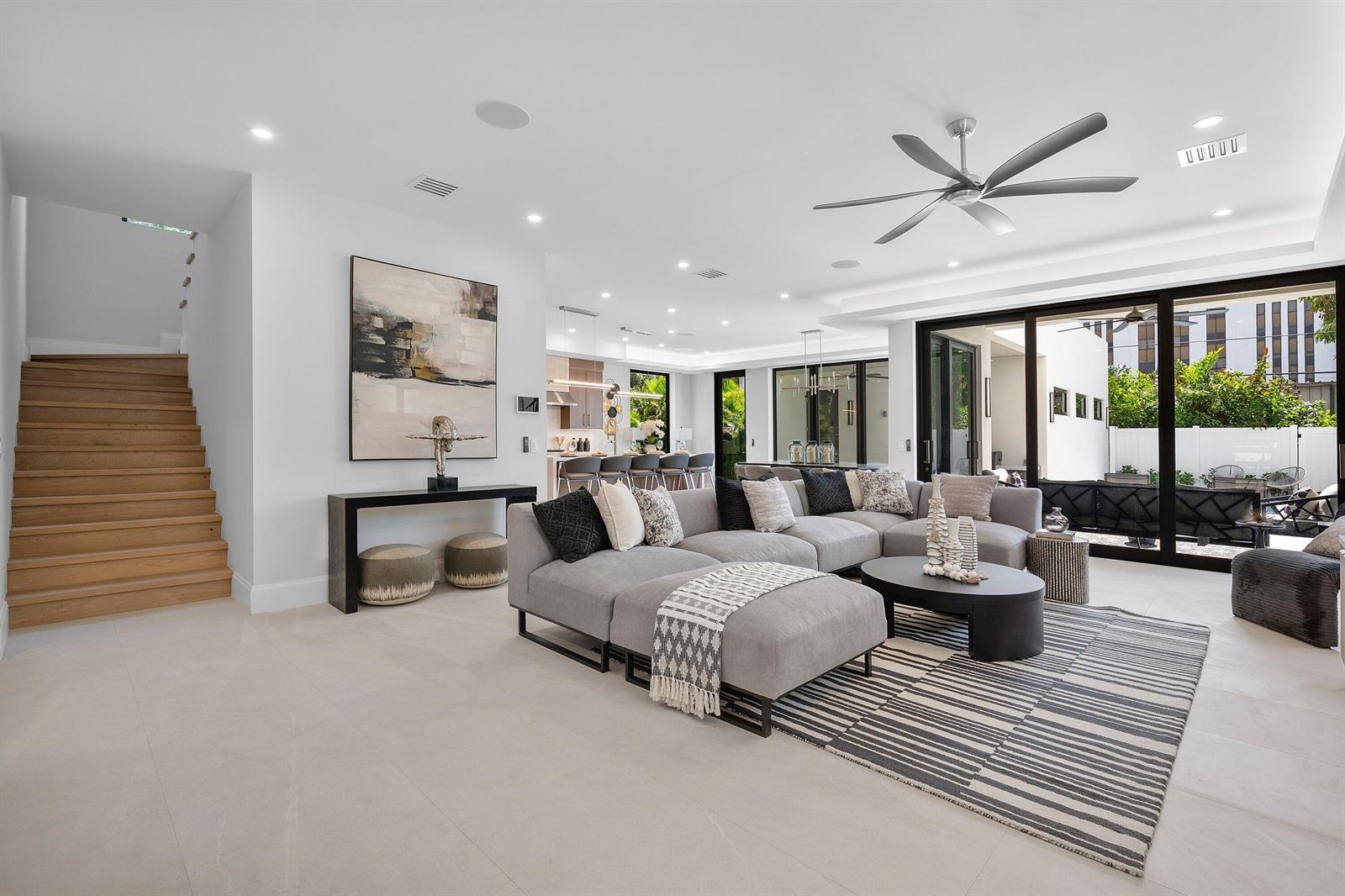 A modern living room features a large gray sectional, wooden stairs, and sliding glass doors — 731 SE 4th Avenue, Delray Beach FL 33483, DELRAY BEACH, FL