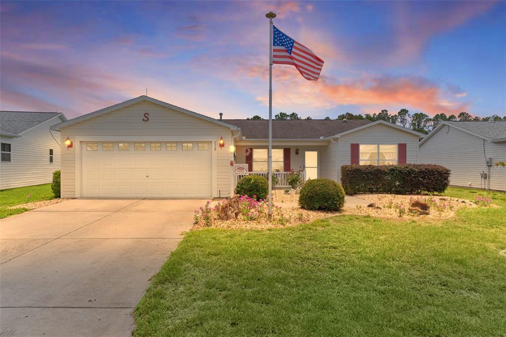 A single-story house with a white garage, a front lawn, and an American flag pole — 1317 CARVELLO DRIVE, THE VILLAGES, FL