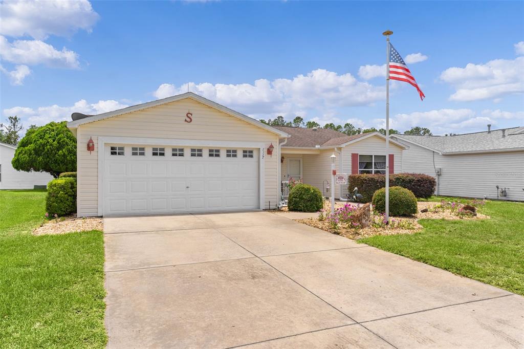 A single-story house with a white garage, beige siding, and an American flag in front — 1317 CARVELLO DRIVE, THE VILLAGES, FL