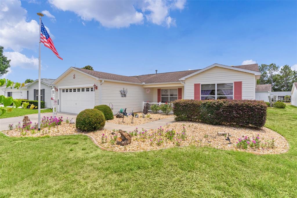 A single-story house with beige siding, a two-car garage, and a landscaped front yard — 1317 CARVELLO DRIVE, THE VILLAGES, FL