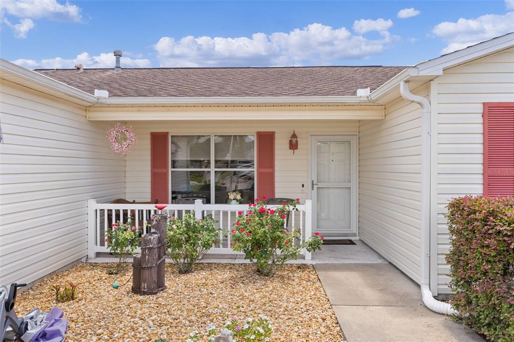 The exterior of a house features beige siding, a small front porch, and a gravel garden — 1317 CARVELLO DRIVE, THE VILLAGES, FL