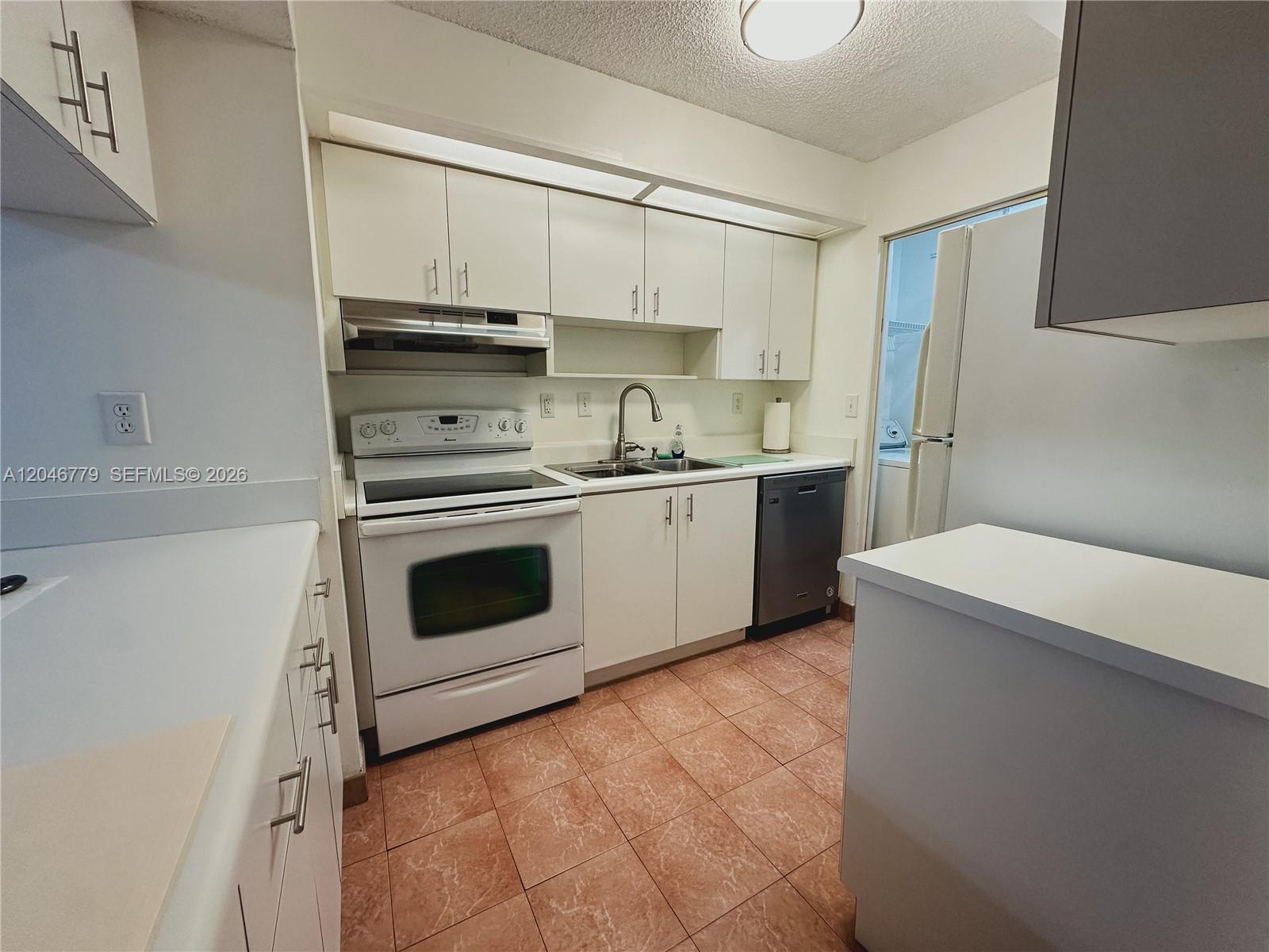 A kitchen features white cabinets, white appliances, a stainless steel dishwasher, and tiled flooring — 927 NE 199th St # 101, Miami FL 33179, MIAMI, FL