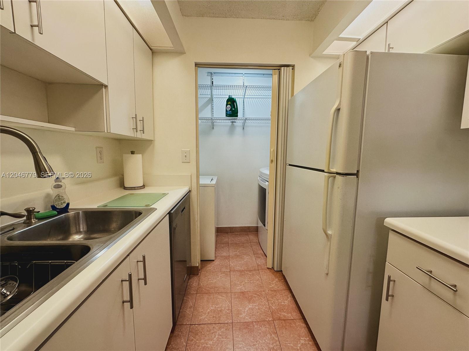 A galley kitchen features white cabinets, a stainless steel sink, and an adjacent laundry closet — 927 NE 199th St # 101, Miami FL 33179, MIAMI, FL