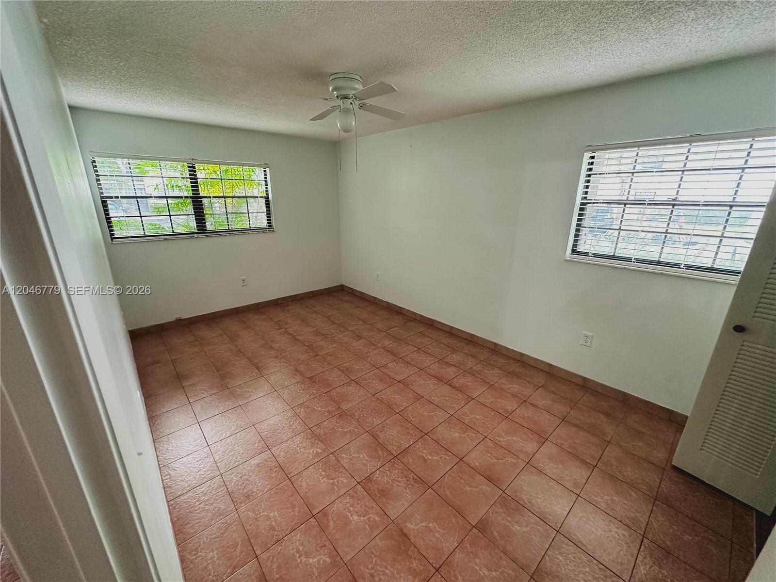 An empty bedroom features white walls, a ceiling fan, and brown tiled flooring — 927 NE 199th St # 101, Miami FL 33179, MIAMI, FL