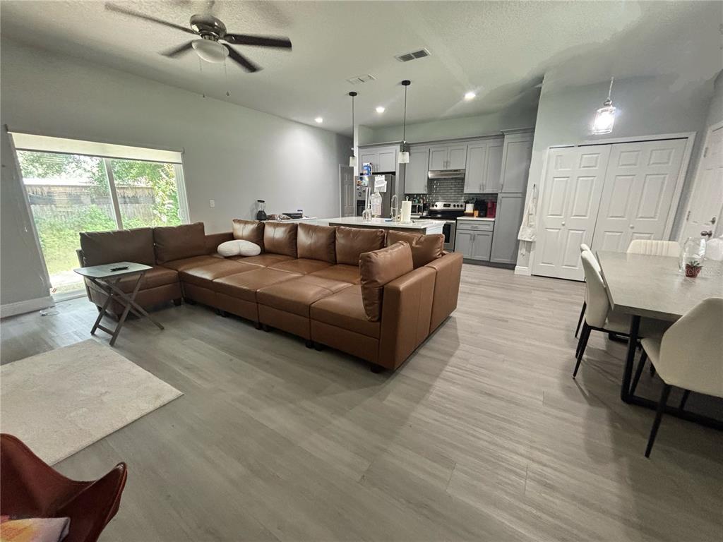 An open-concept living room and kitchen feature gray flooring, a large brown sectional, and cabinetry — 1313 5TH STREET, ORANGE CITY, FL