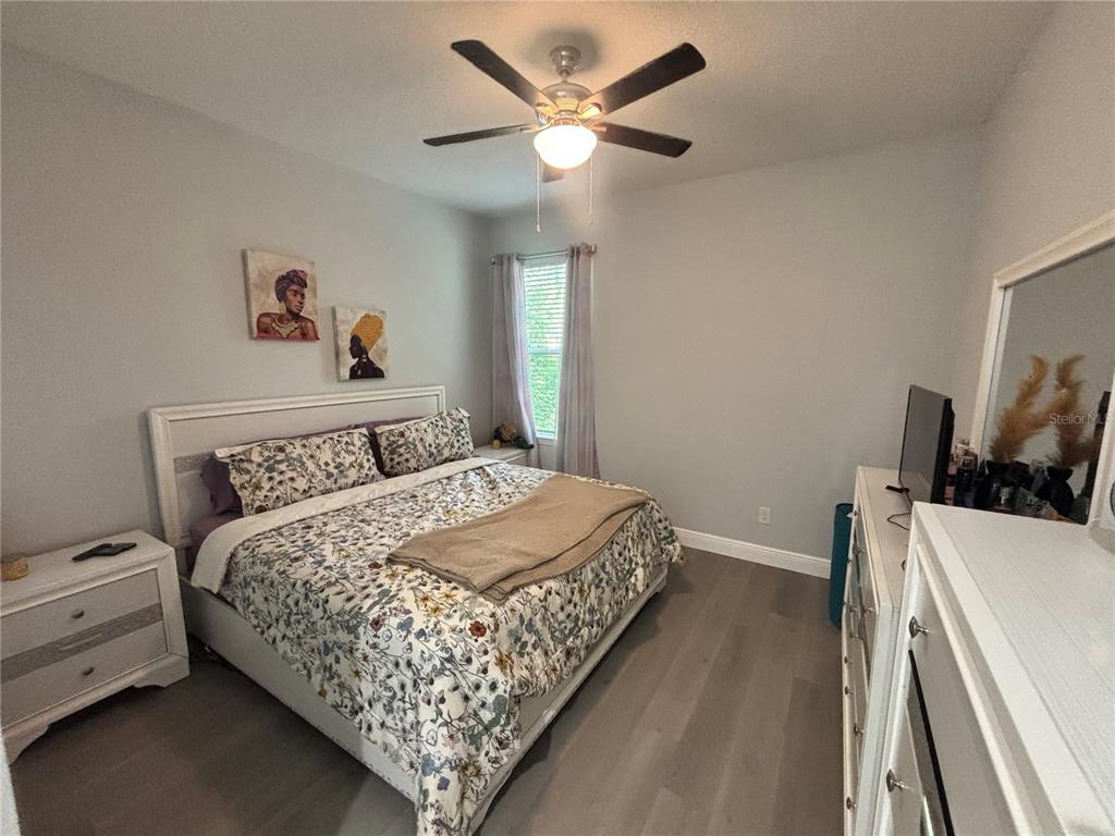 A bedroom features a bed with floral bedding, a ceiling fan, and light wood flooring — 1313 5TH STREET, ORANGE CITY, FL