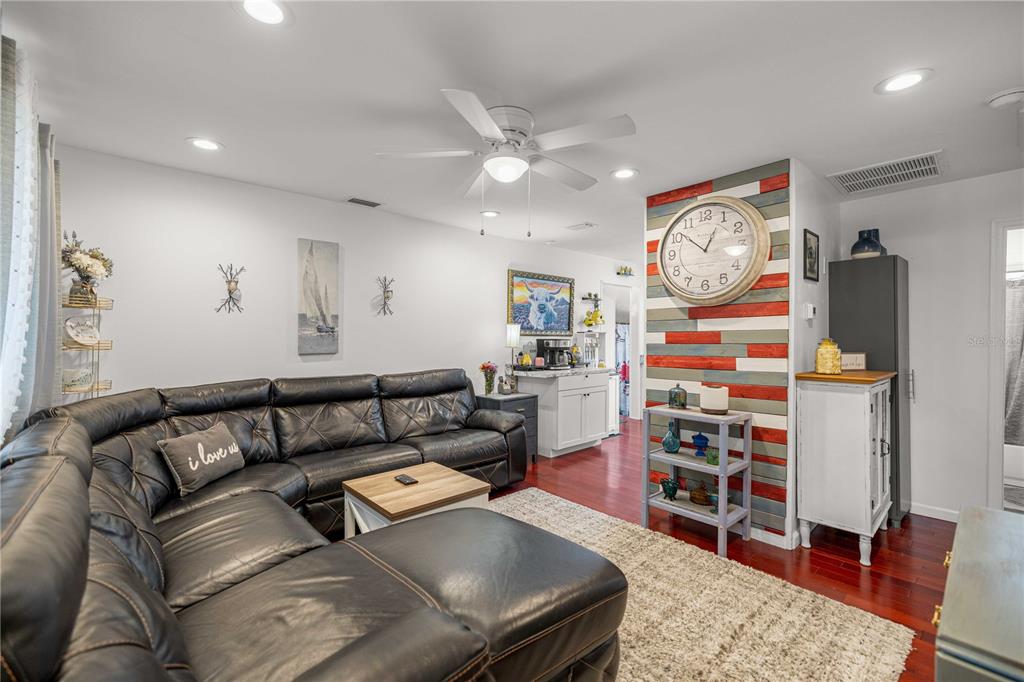 A living room features a black leather sectional, a wood-paneled accent wall, and a large clock — 1512 NE 37TH STREET, OCALA, FL