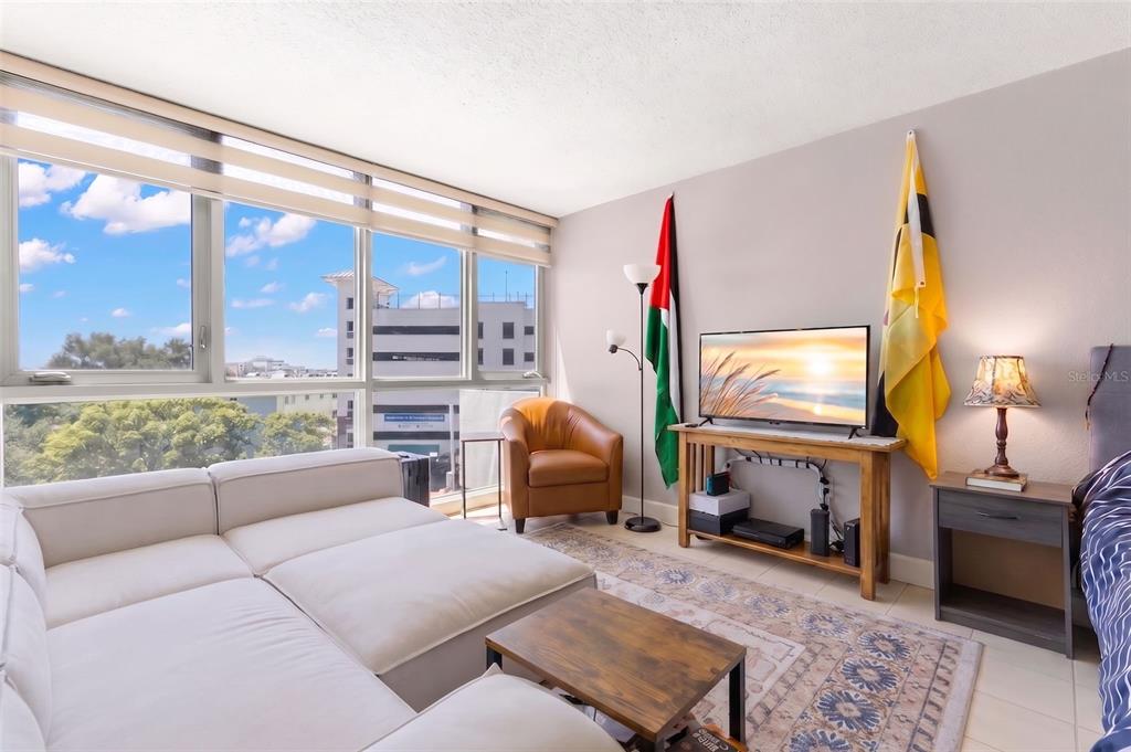 A living room features a white sectional sofa, a television on a wooden stand, and windows — 470 3RD STREET S UNIT 515, ST PETERSBURG, FL