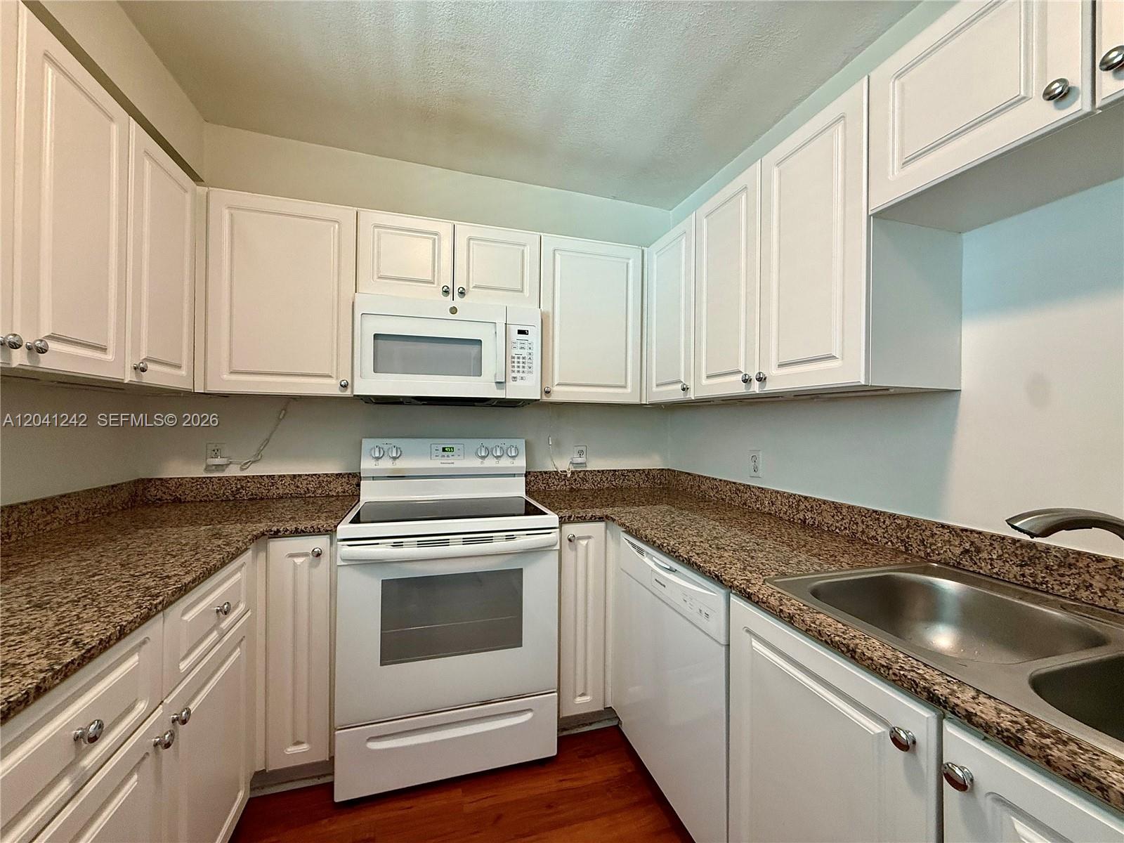 A kitchen features white cabinets, granite countertops, and white appliances — 7800 Collins Ave # 407, Miami Beach FL 33141, MIAMI BEACH, FL