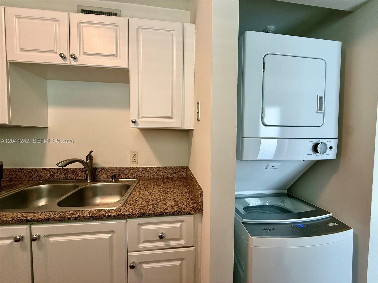 A kitchen sink with granite countertops sits next to a stacked washer and dryer unit — 7800 Collins Ave # 407, Miami Beach FL 33141, MIAMI BEACH, FL