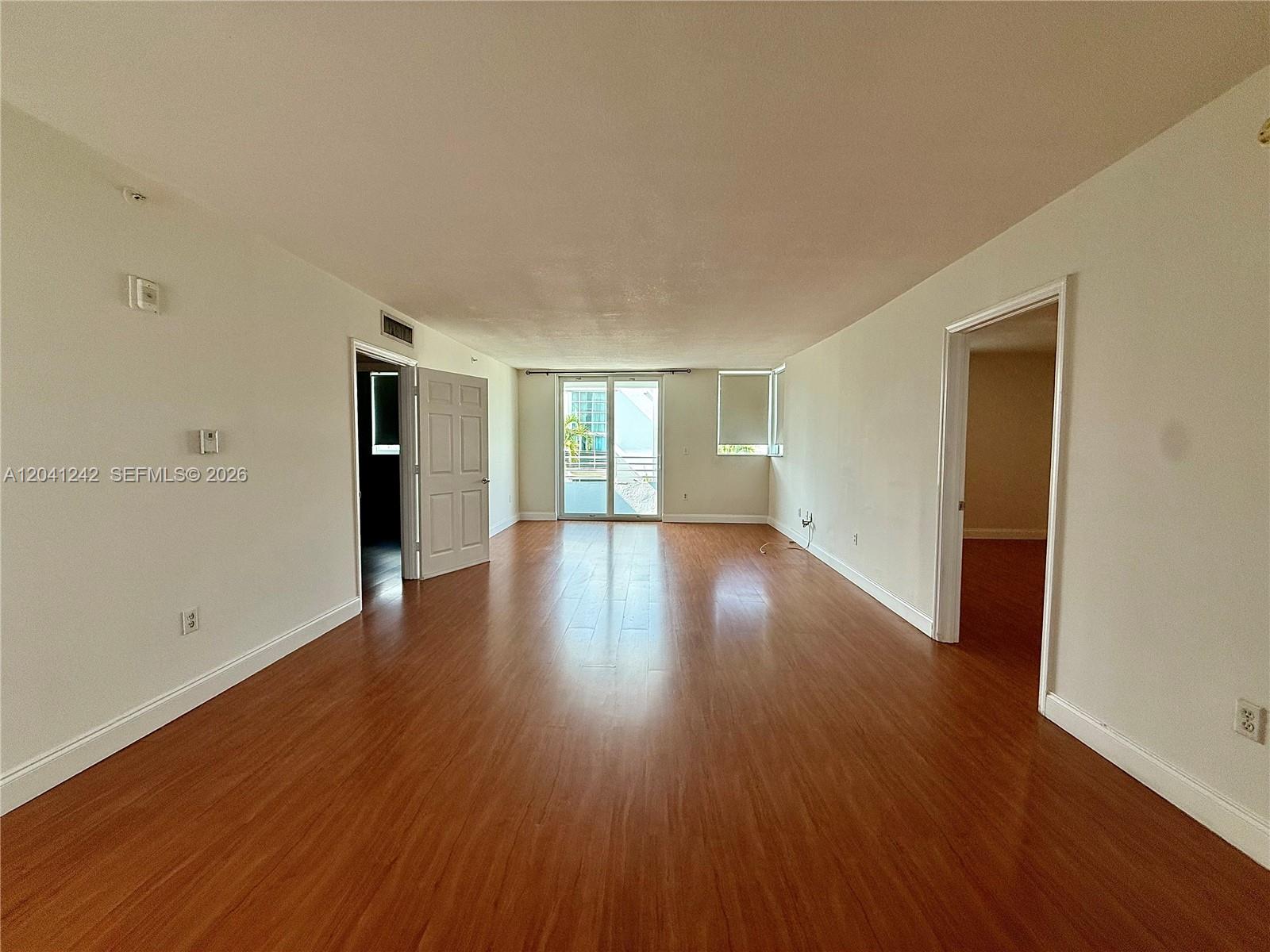 An empty living room features light-colored walls, wood-look flooring, and a sliding glass balcony door — 7800 Collins Ave # 407, Miami Beach FL 33141, MIAMI BEACH, FL