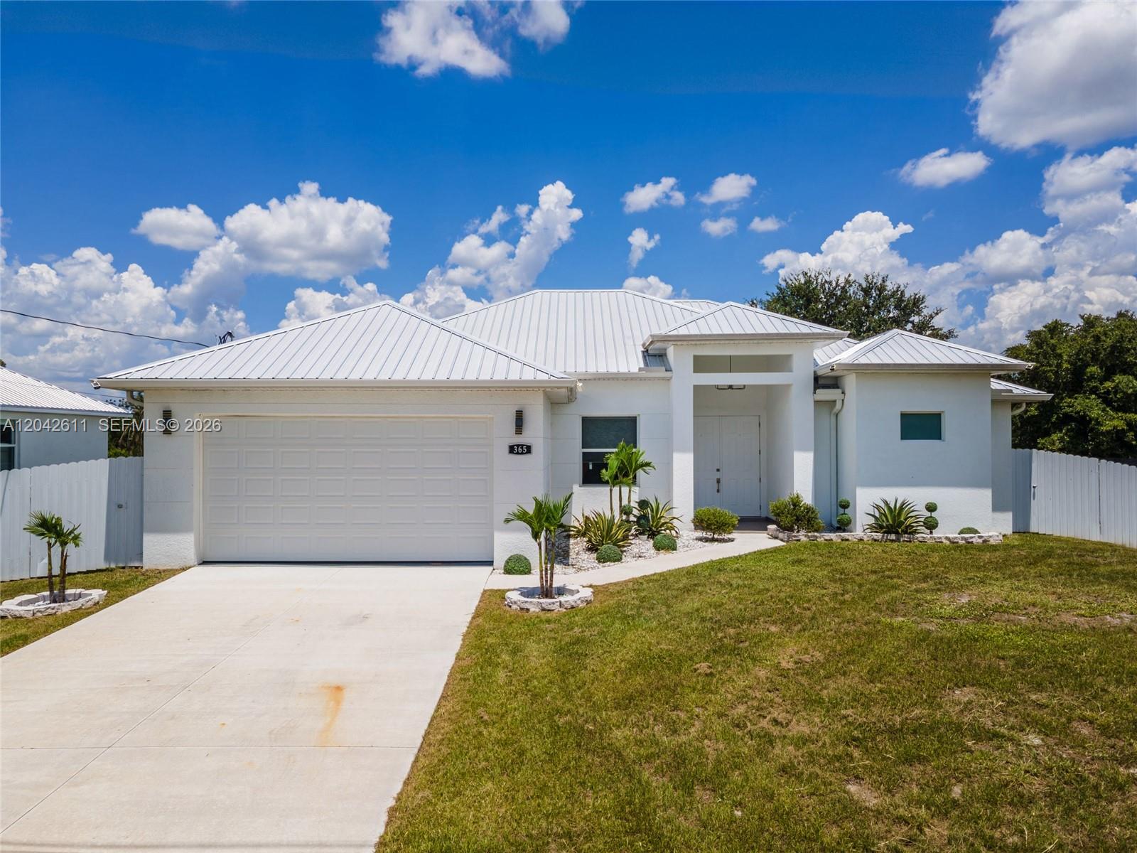A white single-story house features a metal roof, a two-car garage, and a concrete driveway — 365 Ranier Ave, Lehigh Acres FL 33974, LEHIGH ACRES, FL