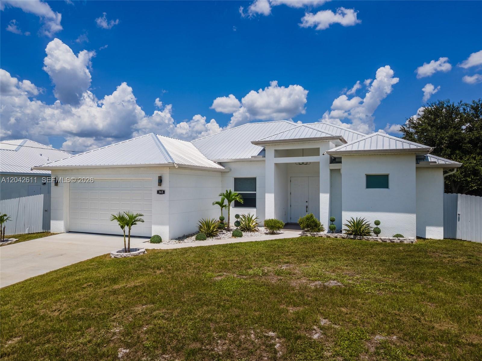 A white single-story house with a metal roof and a two-car garage — 365 Ranier Ave, Lehigh Acres FL 33974, LEHIGH ACRES, FL