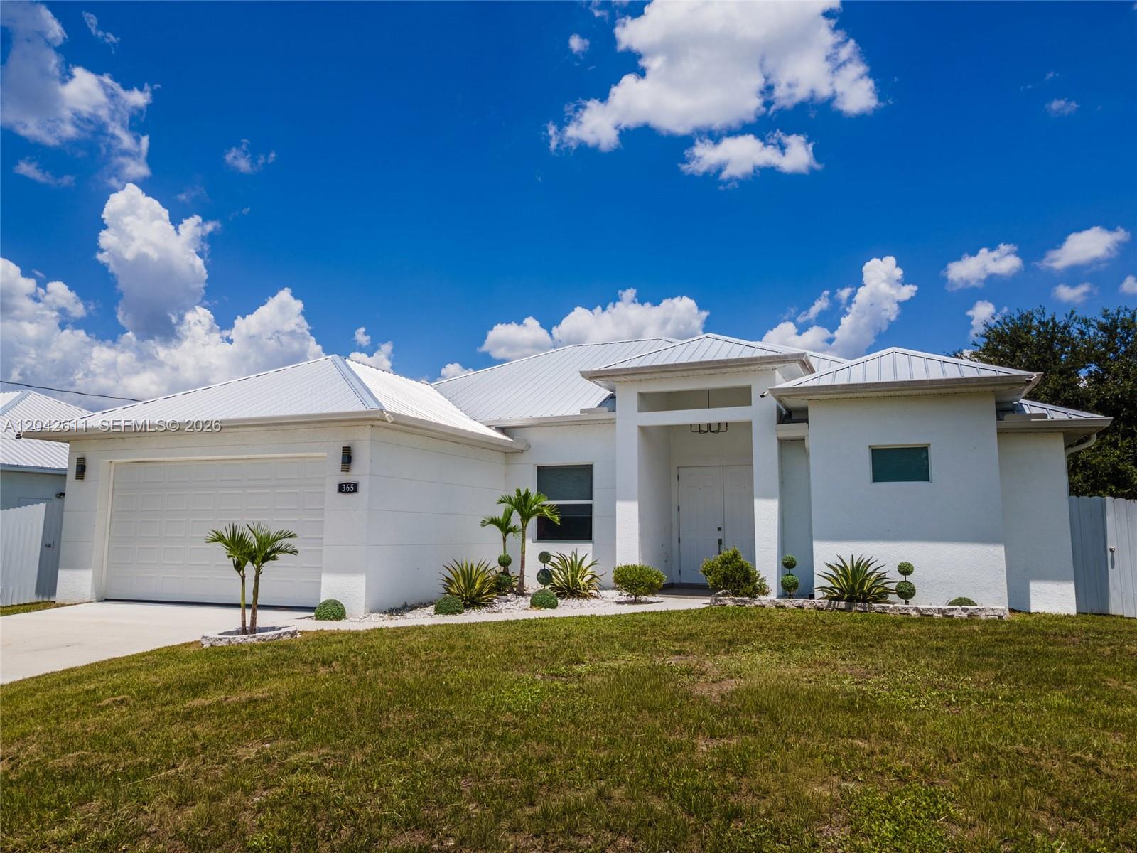 A white single-story house with a metal roof and a two-car garage — 365 Ranier Ave, Lehigh Acres FL 33974, LEHIGH ACRES, FL