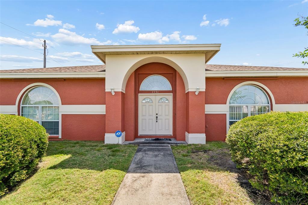 The front exterior of a single-story house features a red stucco facade and arched windows — 7791 CARVER COURT, SEMINOLE, FL