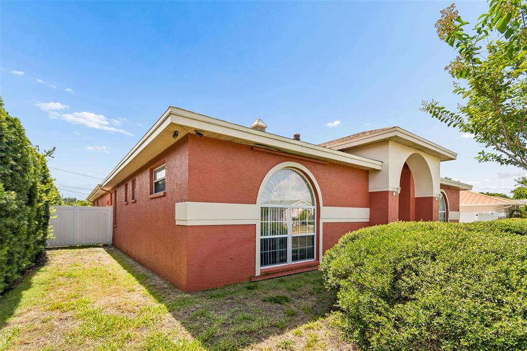 A red stucco house with a white arched window and a white fence on the side — 7791 CARVER COURT, SEMINOLE, FL
