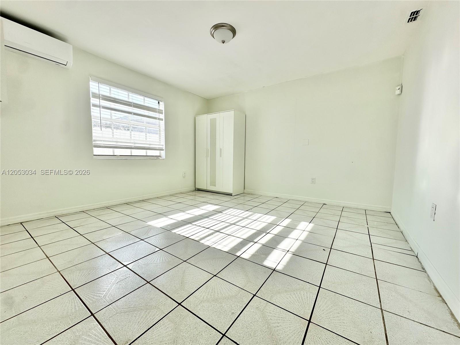 A sparsely furnished room features white walls, a tiled floor, and a window with blinds — 12021 SW 191st St # 2, Miami FL 33177, MIAMI, FL