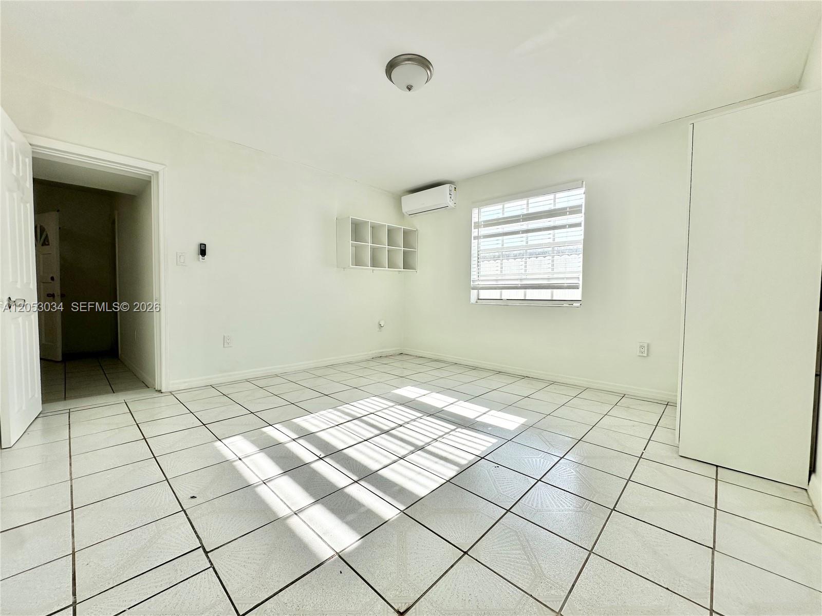 An empty room features white walls, tiled flooring, a window with blinds, and wall-mounted shelving — 12021 SW 191st St # 2, Miami FL 33177, MIAMI, FL