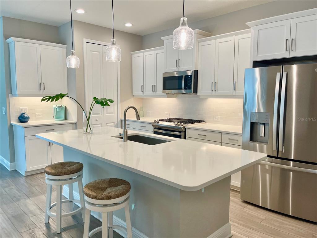 A modern kitchen features white cabinetry, a large quartz island, and stainless steel appliances — 12432 PALATKA DRIVE, VENICE, FL