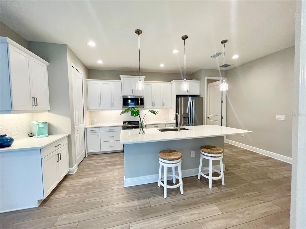 A modern kitchen features white cabinetry, a central island with bar seating, and wood-look flooring — 12432 PALATKA DRIVE, VENICE, FL