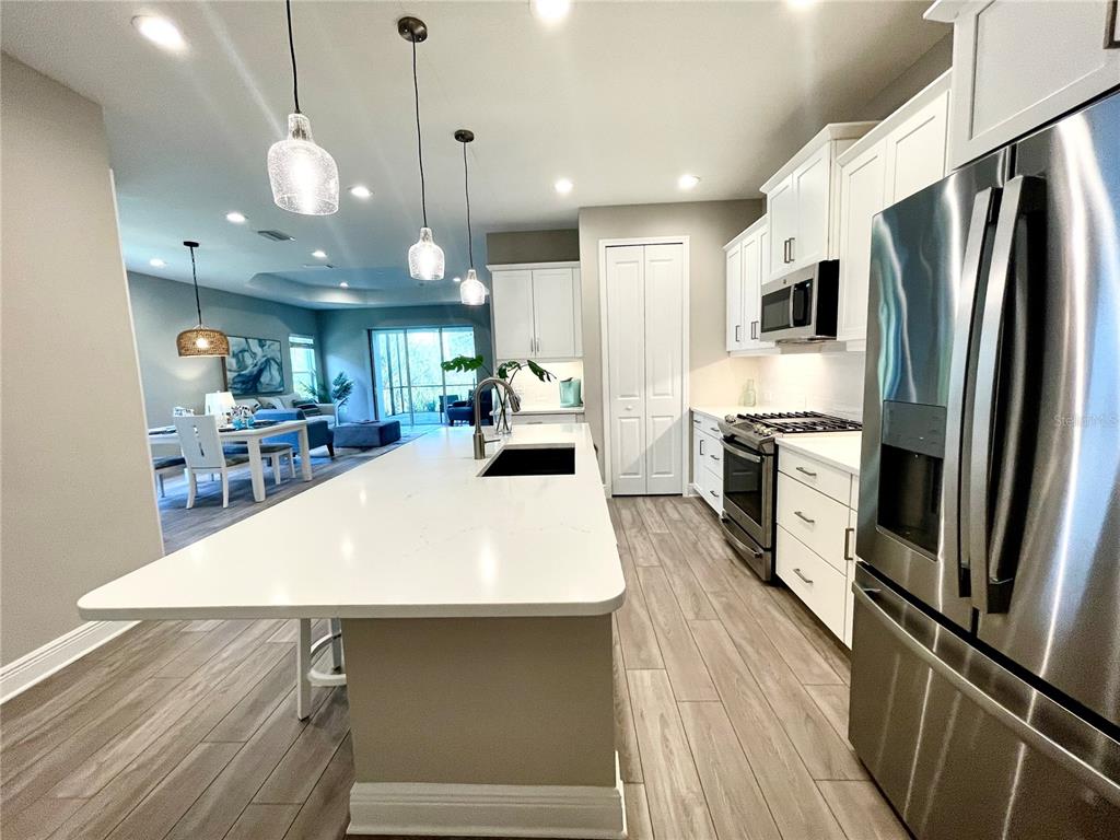 A modern kitchen features a white quartz island, stainless steel appliances, and light wood flooring — 12432 PALATKA DRIVE, VENICE, FL