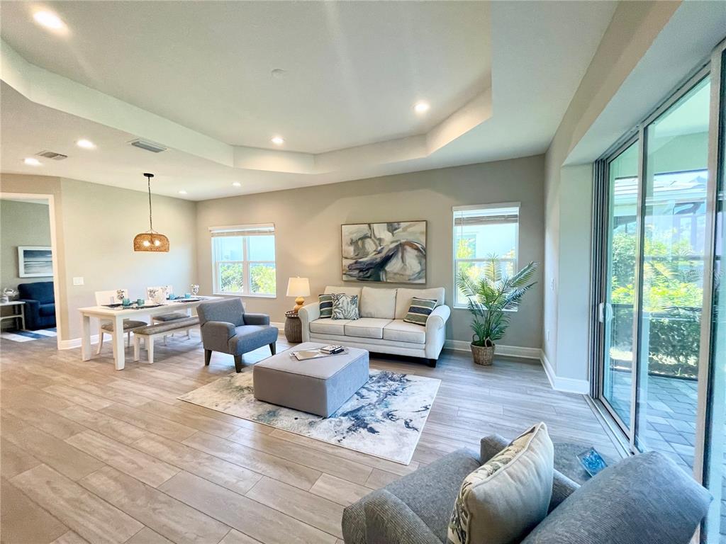 A living and dining area features light wood-look flooring, a tray ceiling, and sliding glass doors — 12432 PALATKA DRIVE, VENICE, FL