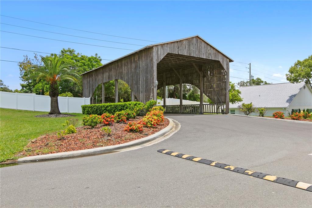 A wooden covered bridge stands over a paved driveway with a speed bump — 6225 ELMHURST DRIVE, NEW PORT RICHEY, FL