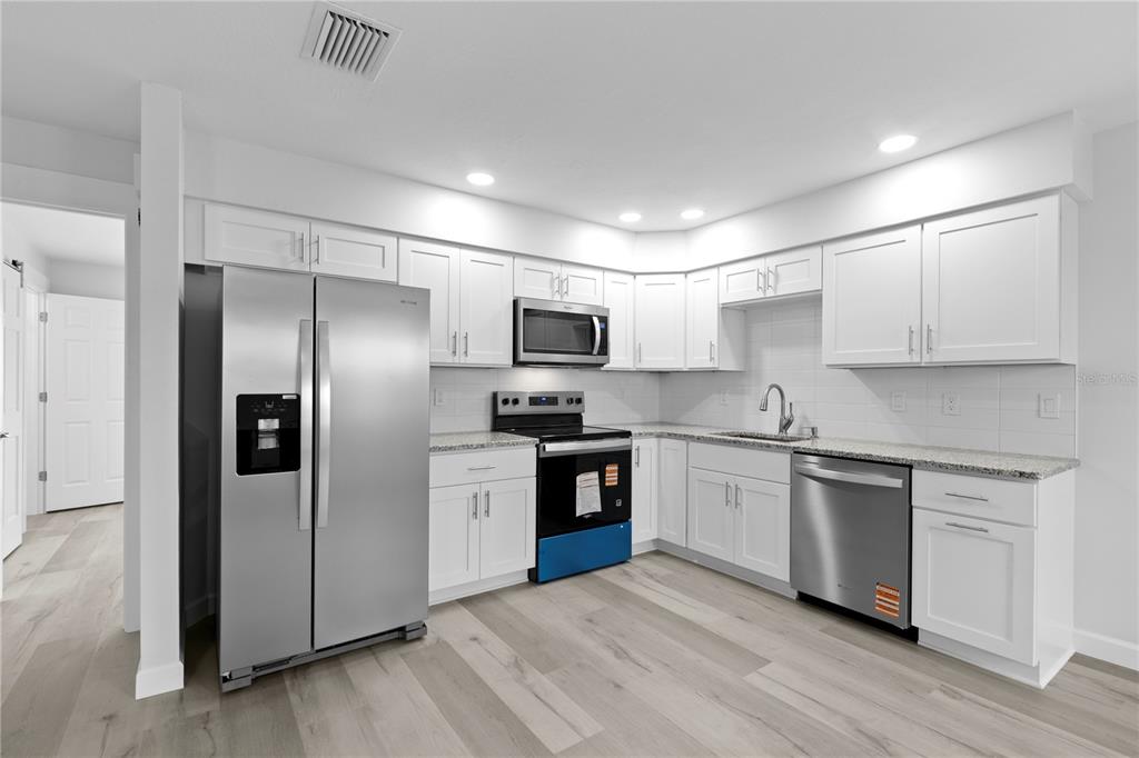 A kitchen with white cabinets, stainless steel appliances, granite countertops, and light wood-look flooring — 6225 ELMHURST DRIVE, NEW PORT RICHEY, FL