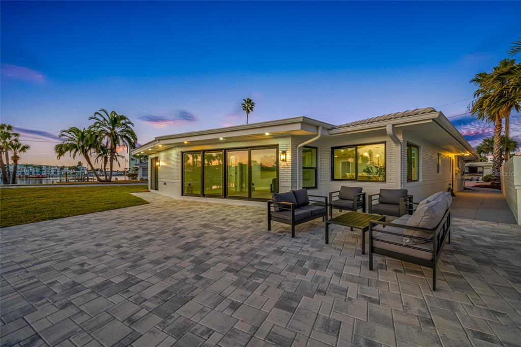 A paved patio with outdoor seating sits outside a white house with large glass doors — 370 59TH AVENUE, ST PETE BEACH, FL