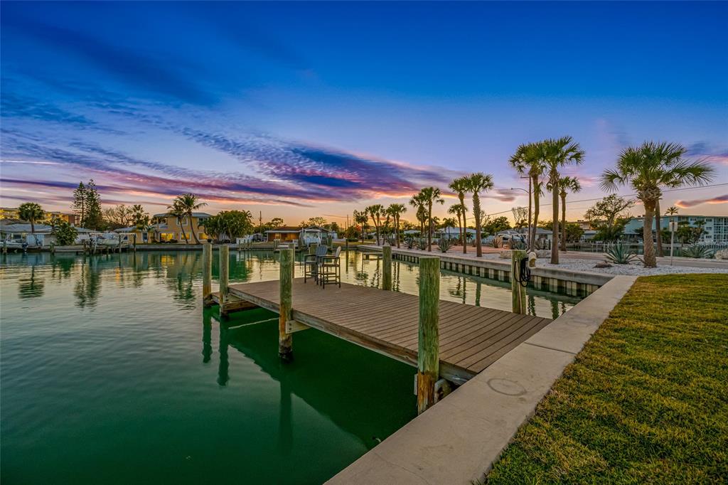 A wooden dock extends into a calm canal at sunset with palm trees nearby — 370 59TH AVENUE, ST PETE BEACH, FL