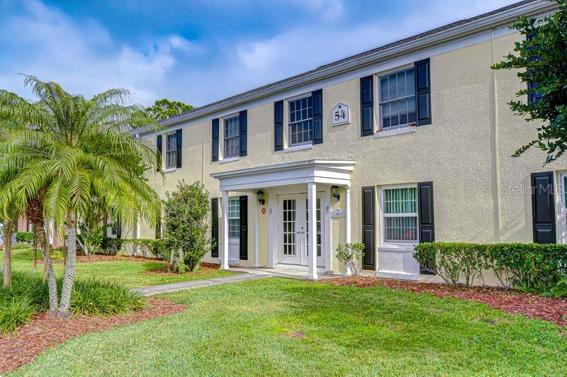 A two-story apartment building with beige stucco walls, black shutters, and a palm tree — 13693 ORANGE SUNSET DRIVE UNIT 203, TAMPA, FL