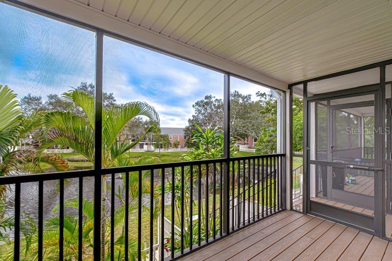 A screened-in porch with wood-look flooring overlooks a pond and a residential neighborhood — 13693 ORANGE SUNSET DRIVE UNIT 203, TAMPA, FL