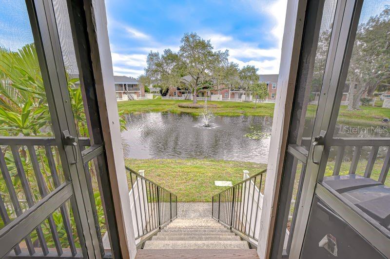 A view from a screened porch looking down stairs toward a pond with a fountain — 13693 ORANGE SUNSET DRIVE UNIT 203, TAMPA, FL