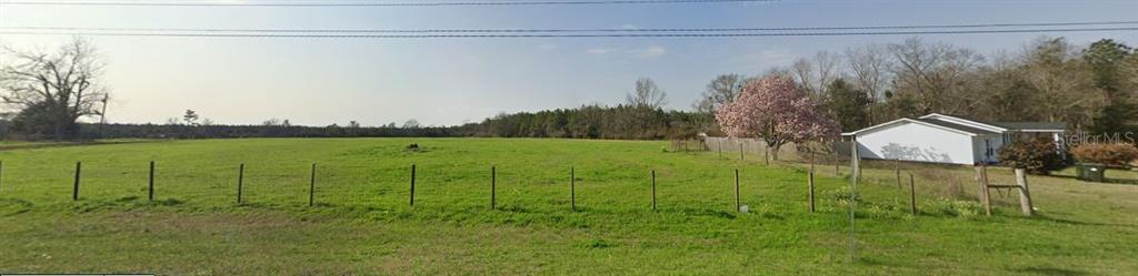 A wide, grassy field is bordered by a wire fence and a white house — 3800 HIGHWAY 99, CENTURY, FL