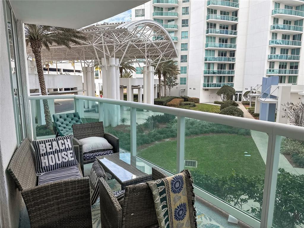 A balcony with wicker furniture overlooks a courtyard and a large modern apartment building — 231 RIVERSIDE DRIVE UNIT 208-1, HOLLY HILL, FL