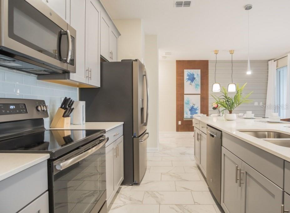 A modern kitchen features gray cabinets, stainless steel appliances, white countertops, and light tile flooring — 468 OCEAN COURSE AVENUE, DAVENPORT, FL