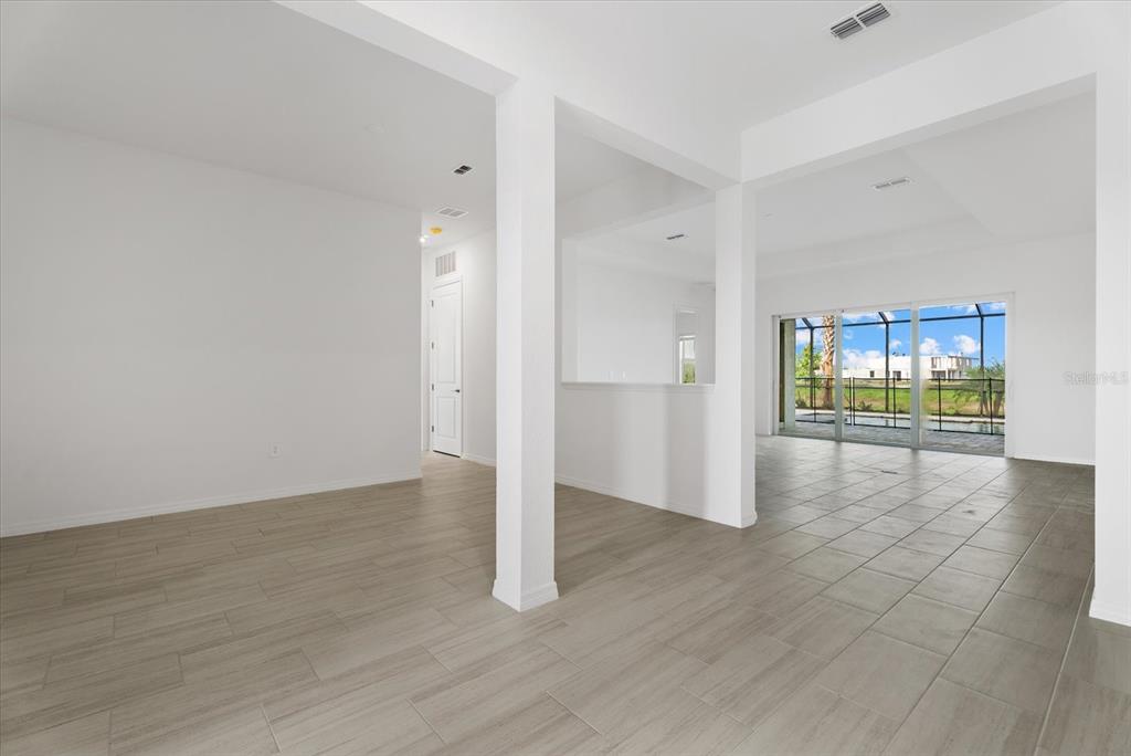 An open-concept living area features white walls, light wood-look tile flooring, and sliding glass doors — 5918 MOUND KEY RUN, LAKEWOOD RANCH, FL