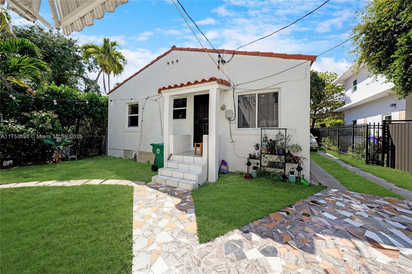 A small, white, single-story house features a tiled entryway, a stone walkway, and a grassy yard — 4727 NE 1st Ct, Miami FL 33137, MIAMI, FL
